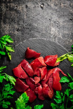 Pieces of raw liver on a stone tray with parsley. On a black background. High quality photo
