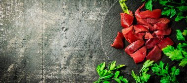 Pieces of raw liver on a stone tray with parsley. On a black background. High quality photo