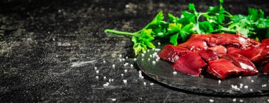 Pieces of raw liver on a stone tray with parsley. On a black background. High quality photo