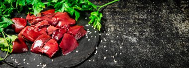 Pieces of raw liver on a stone tray with parsley. On a black background. High quality photo