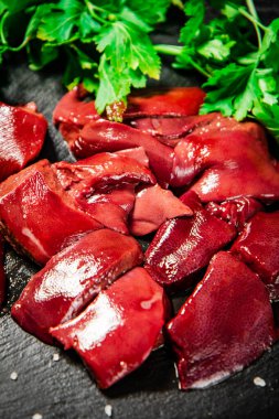Pieces of raw liver on a stone tray with parsley. On a black background. High quality photo
