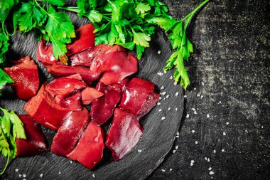 Pieces of raw liver on a stone tray with parsley. On a black background. High quality photo