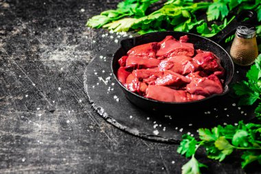 Pieces of raw liver in a frying pan with parsley and spices. On a black background. High quality photo