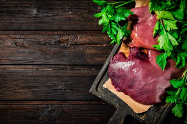 Raw liver on a cutting board on paper. On a wooden background. High quality photo