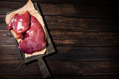 Raw liver on a cutting board on paper. On a wooden background. High quality photo
