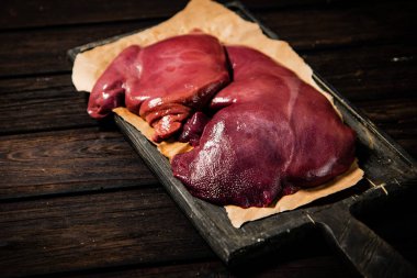 Raw liver on a cutting board on paper. On a wooden background. High quality photo