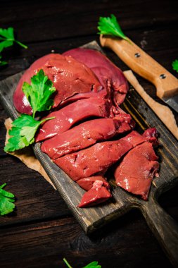 Fresh raw liver on a cutting board with parsley and a knife. On a wooden background. High quality photo