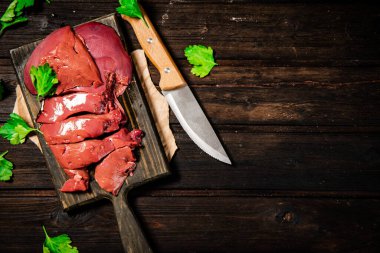 Fresh raw liver on a cutting board with parsley and a knife. On a wooden background. High quality photo