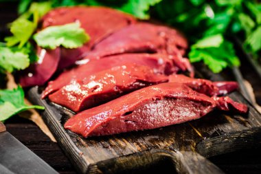 Fresh raw liver on a cutting board with parsley and a knife. On a wooden background. High quality photo