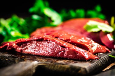 Raw liver on a cutting board with parsley. On a black background. High quality photo