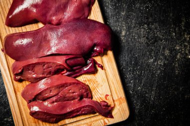 Pieces of raw liver on a wooden cutting board. On a black background. High quality photo