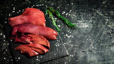 Raw liver on a stone board with rosemary and salt. On a black background. High quality photo