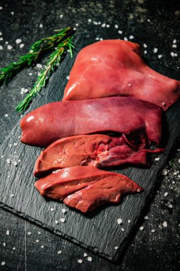 Raw liver on a stone board with rosemary and salt. On a black background. High quality photo