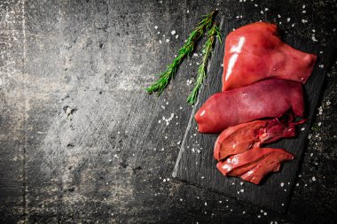 Raw liver on a stone board with rosemary and salt. On a black background. High quality photo