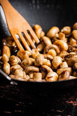 Small fried mushrooms in a frying pan. Against a dark background. High quality photo