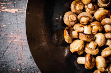 Fried small mushrooms in a frying pan. On a rustic dark background. High quality photo