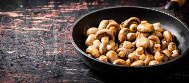 Fried small mushrooms in a frying pan. On a rustic dark background. High quality photo