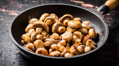 Fried small mushrooms in a frying pan. On a rustic dark background. High quality photo