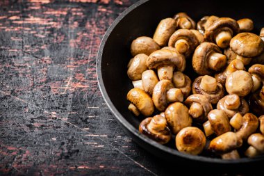 Fried small mushrooms in a frying pan. On a rustic dark background. High quality photo