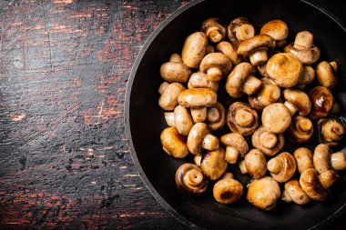 Fried small mushrooms in a frying pan. On a rustic dark background. High quality photo