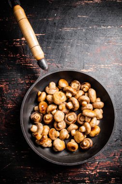 Fried small mushrooms in a frying pan. On a rustic dark background. High quality photo