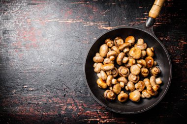 Fried small mushrooms in a frying pan. On a rustic dark background. High quality photo