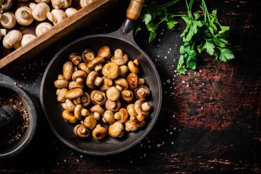 Frying pan with fried small mushrooms with parsley. Against a dark background. High quality photo