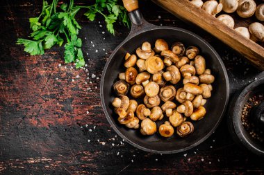 Frying pan with fried small mushrooms with parsley. Against a dark background. High quality photo
