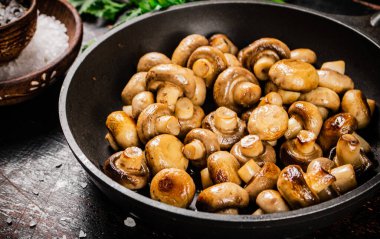Fried small mushrooms in a frying pan. On a rustic dark background. High quality photo