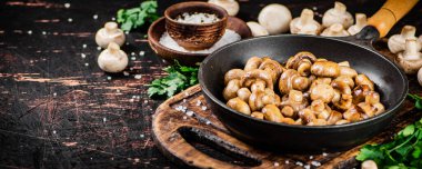 Frying pan with fried small mushrooms with parsley. Against a dark background. High quality photo