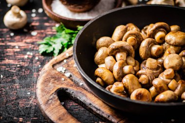 Frying pan with fried small mushrooms with parsley. Against a dark background. High quality photo
