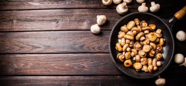 Delicious small fried mushrooms in a frying pan. On a wooden background. High quality photo