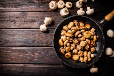 Delicious small fried mushrooms in a frying pan. On a wooden background. High quality photo