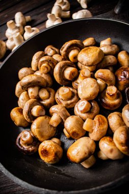 Delicious small fried mushrooms in a frying pan. On a wooden background. High quality photo