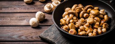 Fragrant homemade fried mushrooms in a frying pan on a cutting board. On a wooden background. High quality photo