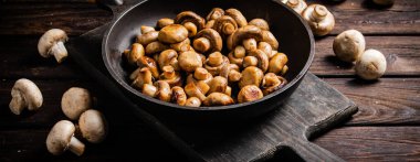 Fragrant homemade fried mushrooms in a frying pan on a cutting board. On a wooden background. High quality photo