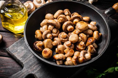 Fragrant homemade fried mushrooms in a frying pan on a cutting board. On a wooden background. High quality photo