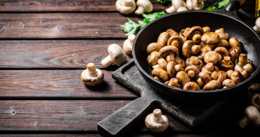 Fragrant homemade fried mushrooms in a frying pan on a cutting board. On a wooden background. High quality photo