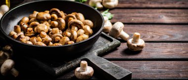 Fragrant homemade fried mushrooms in a frying pan on a cutting board. On a wooden background. High quality photo