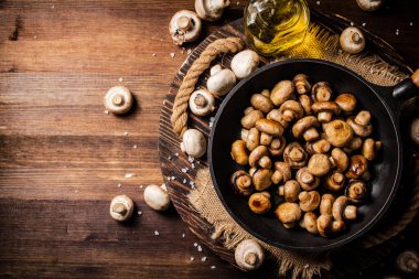 Frying pan with fried mushrooms on a wooden tray. On a wooden background. High quality photo