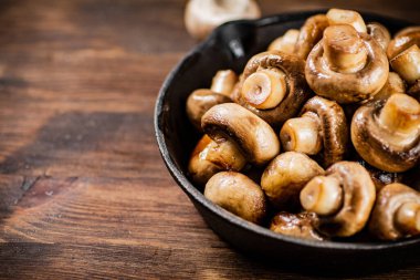 A frying pan with fried mushrooms on the table. On a wooden background. High quality photo