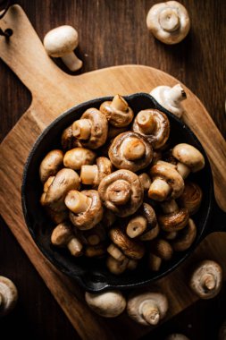 Fried mushrooms in a frying pan on a cutting board. On a wooden background. High quality photo