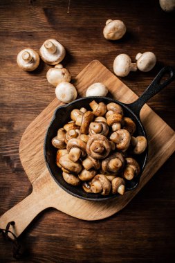 Fried mushrooms in a frying pan on a cutting board. On a wooden background. High quality photo