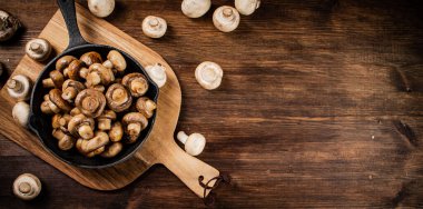 Fried mushrooms in a frying pan on a cutting board. On a wooden background. High quality photo