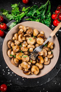 Fried mushrooms in a bowl with greens and tomatoes on a stone board. On a black background. High quality photo
