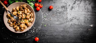 Fried mushrooms in a bowl with greens and tomatoes on a stone board. On a black background. High quality photo