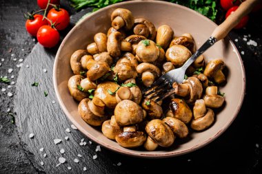 Fried mushrooms in a bowl with greens and tomatoes on a stone board. On a black background. High quality photo