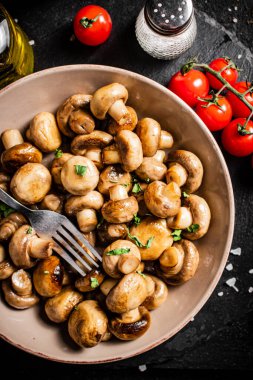 Fried mushrooms in a bowl with cherry tomatoes. On a black background. High quality photo