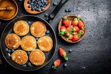 Pancakes in a frying pan with fresh berries and honey. On a black background. High quality photo