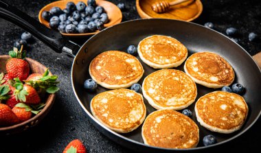 Pancakes in a frying pan with fresh berries and honey. On a black background. High quality photo